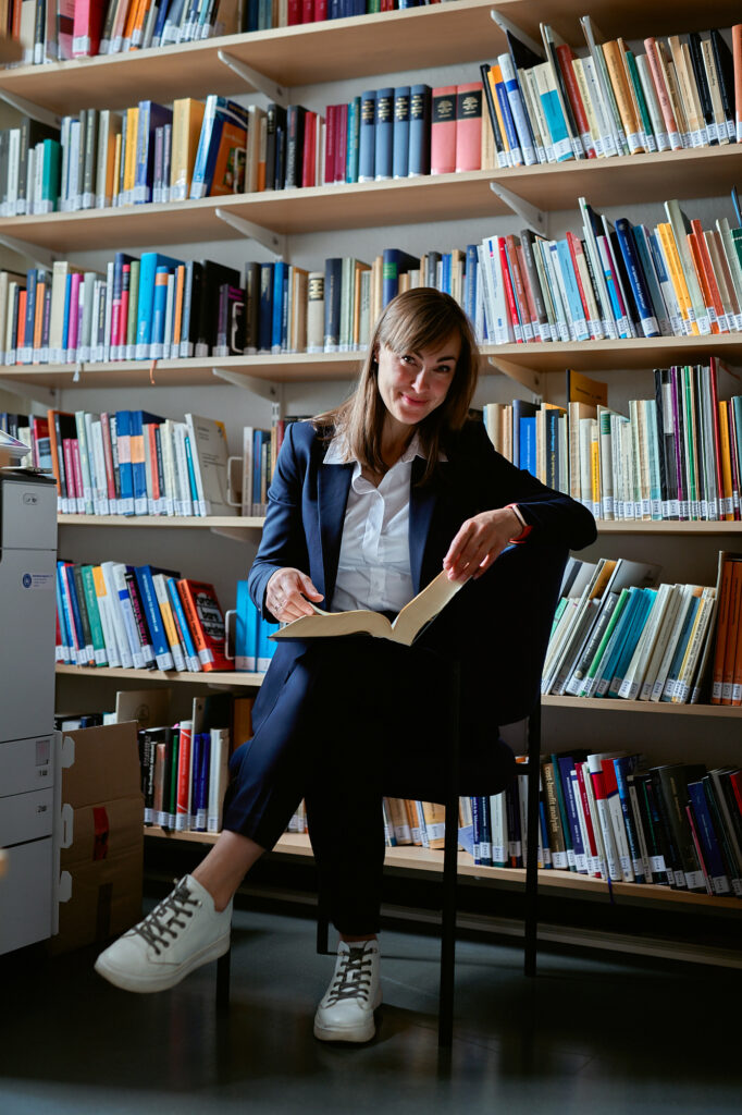 Dariia Opryshko sitzt mit einem Buch vor einem Bücherregal