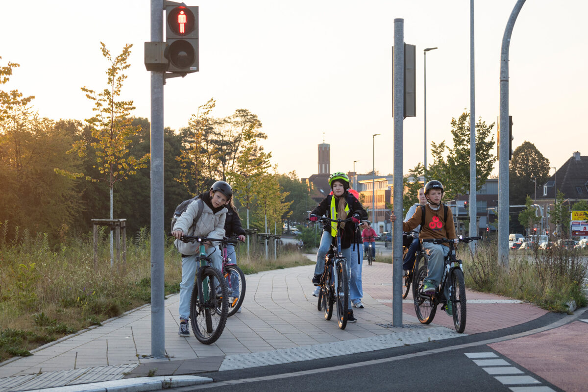 Die Kinder Jakob Wagemann, Maxim Wrobel und Lilli Krause stehen mit ihren Fahrrädern an einer roten Ampel.