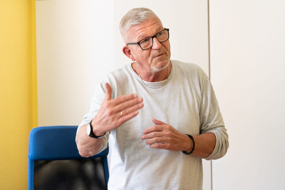 Lothar Bardenhorst sitzt in einem schwarzen Sessel vor gelber Wand