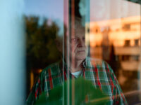 Horst Eschler guckt durch Wohnzimmerfenster zum Balkon raus