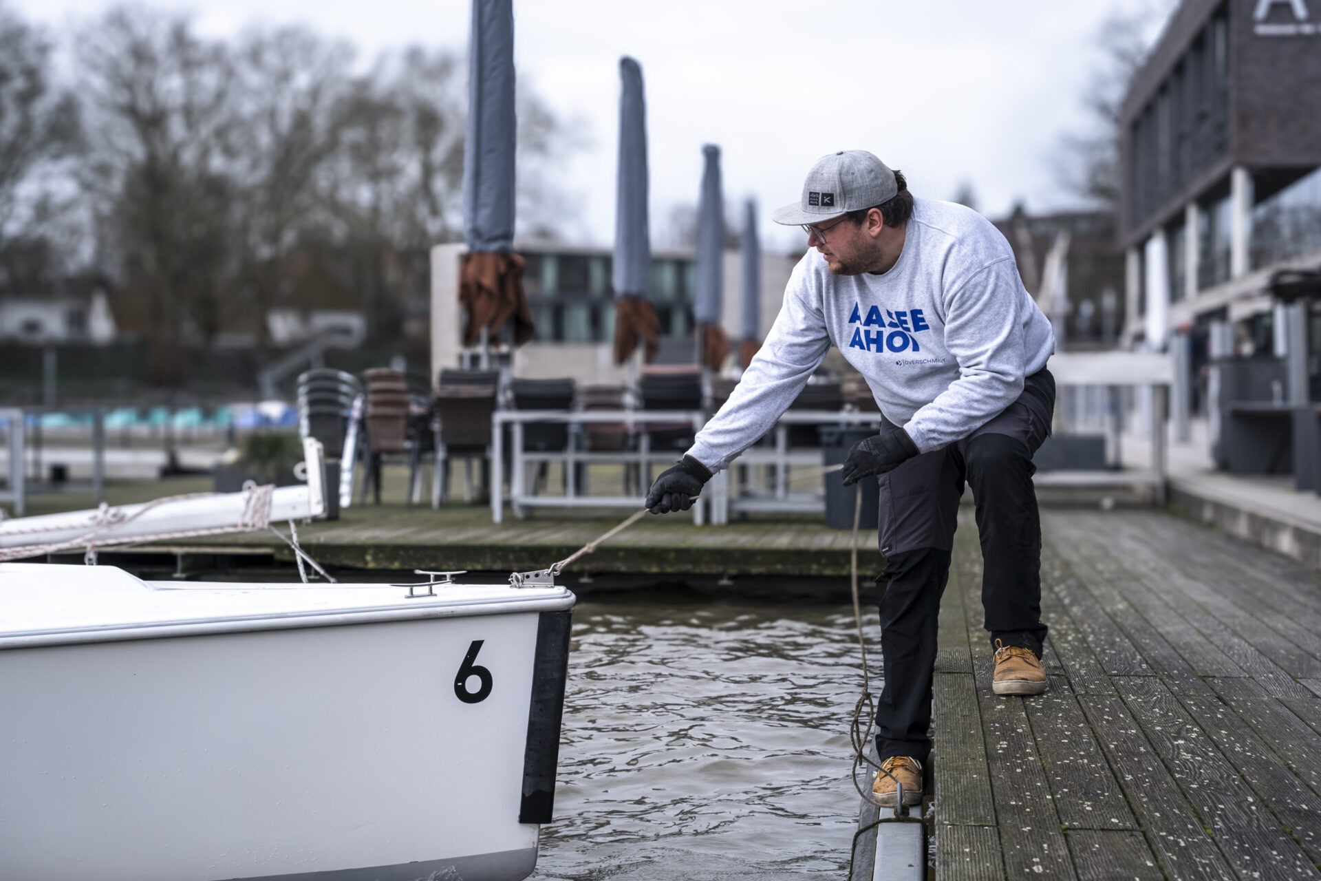 Vor der Segelschule macht Simon Bitter die Mariner 600 mit der Vorleine fest. Die neuesten Boote kommen nach vorne, wo sie besser zu sehen sind. In den Tagen darauf setzt das Segelschul-Team die Masten und befestigt daran die Segel. Simon macht mit der Vorleine das Boot vom Typ Mariner 600 direkt vor der Segelschule fest
