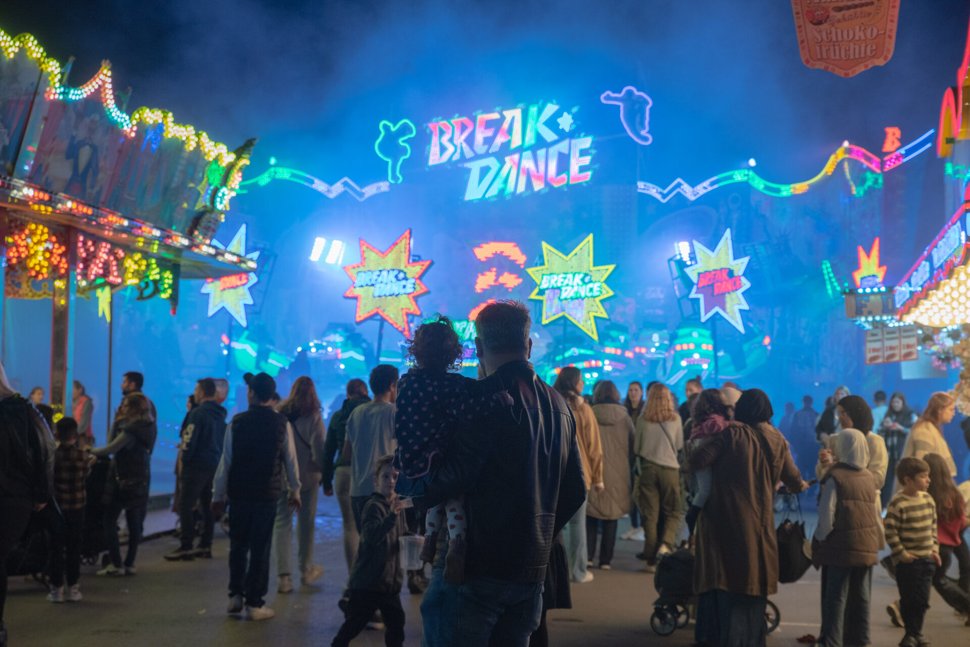 Im Vordergrund Send-Besucher:innen, hinten ein leuchtender Schriftzug "Break Dance" in der Nacht