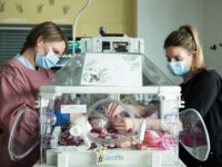 Auf der Frühchenstation schauen 2 Frauen auf das Baby im Inkubator