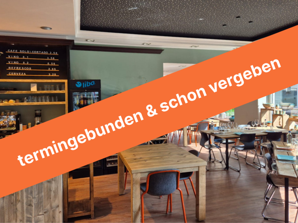 Das Restaurant Olive und Meer mit Holztischen, Stühlen und einem Regal voller Weine. An der Wand stehen Getränkepreise und eine Getränkekühltruhe ist zu sehen. Über dem Bild liegt ein oranger Balken mit der Aufschrift termingebunden & schon vergeben.