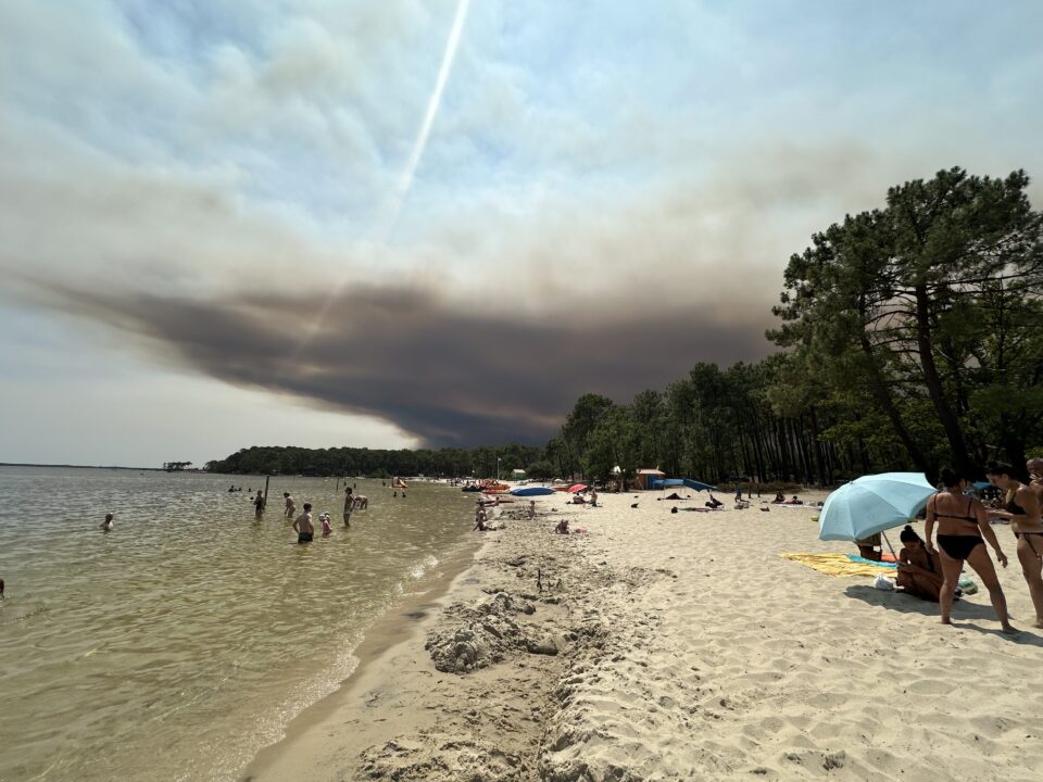 Das Bild zeigt einen Strand in der Nähe von Carcans, über dem Himmel machen sich schwarze Rauchwolken breit, weil die Region von schweren Waldbränden getroffen ist.