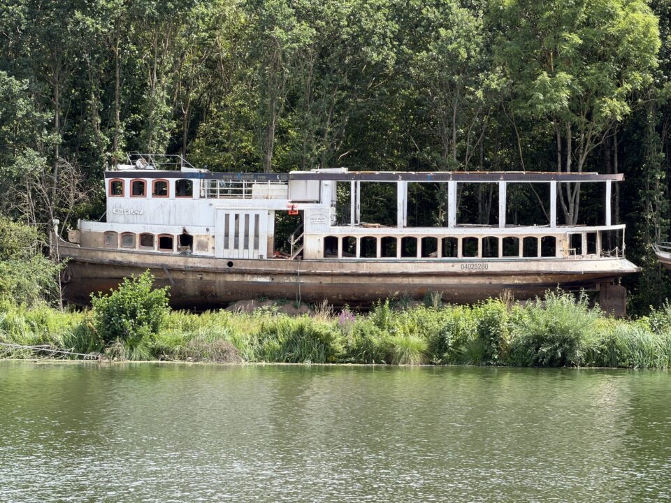 Ein verrostetes Schiff liegt am Ufer neben der Saar.